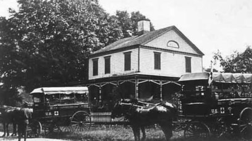 A vintage black-and-white photograph of the historic Brownson House, a two-story clapboard home with a full-width porch, flanked by horse-drawn carriages