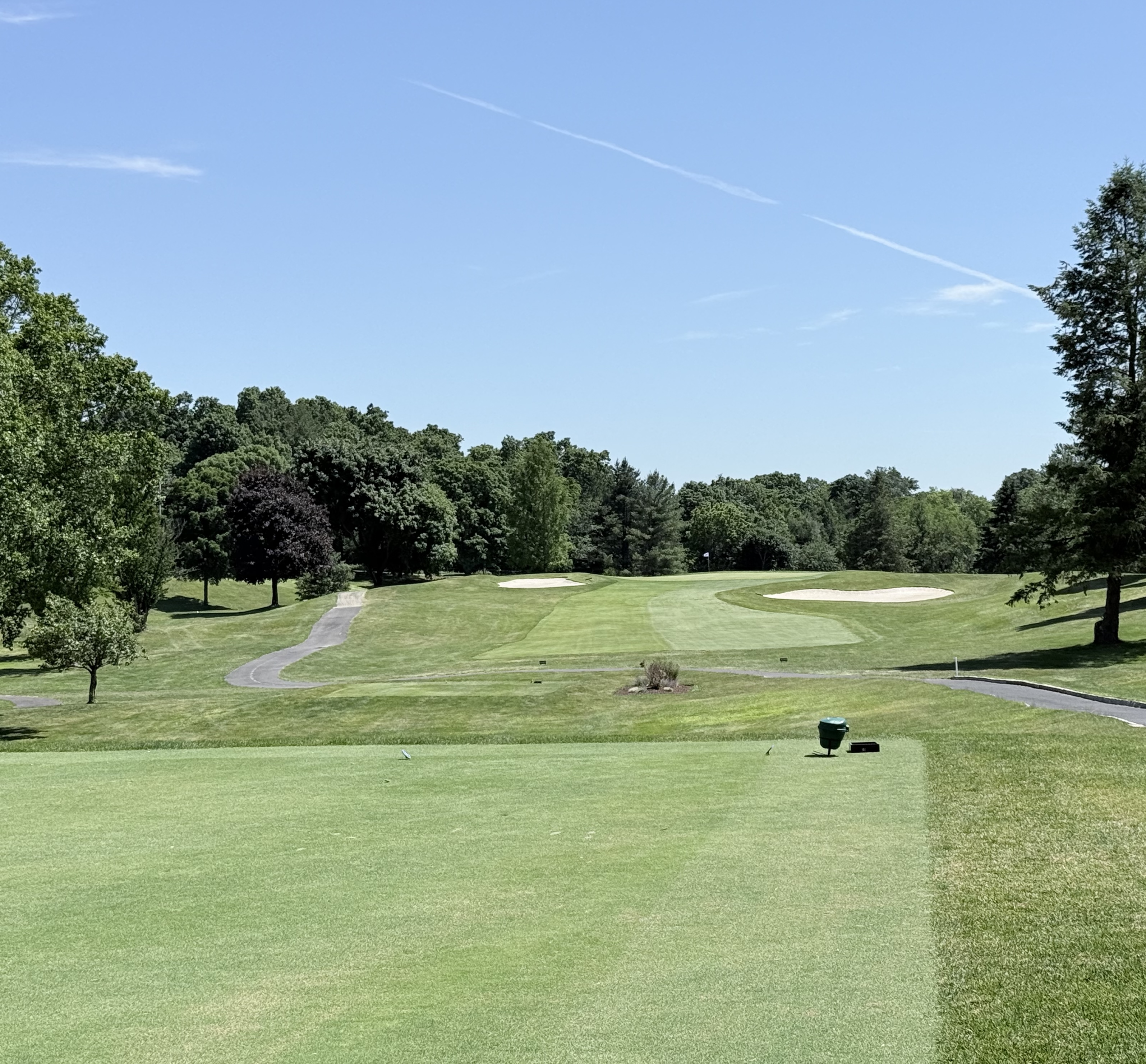 View down a Brownson Country Club golf hole from the tee box, showing the fairway, cart path, and an elevated green flanked by sand bunkers framed by mature trees