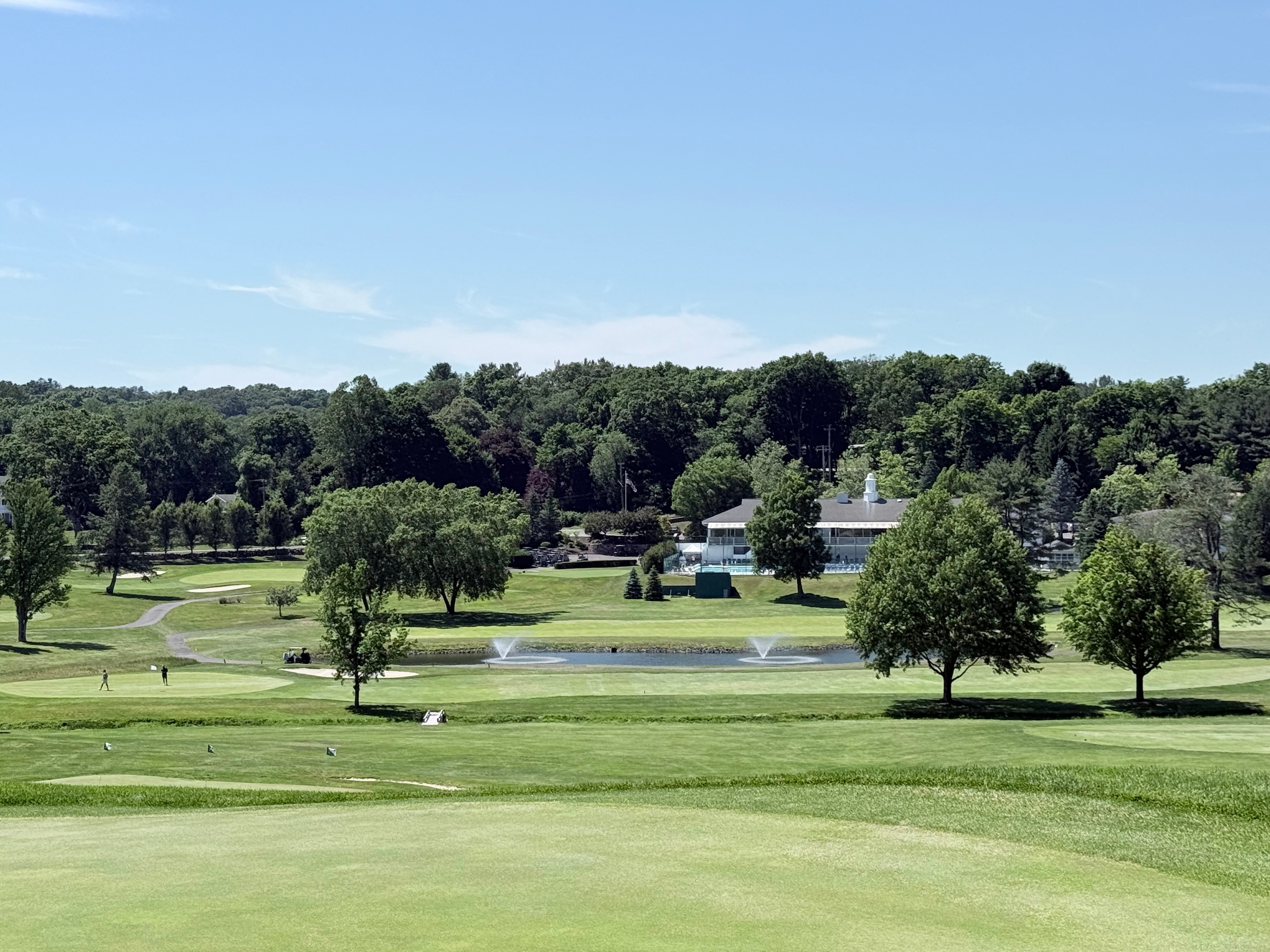 Scenic view from the 7th green at Brownson Country Club, overlooking a pond with fountains toward the clubhouse and pool