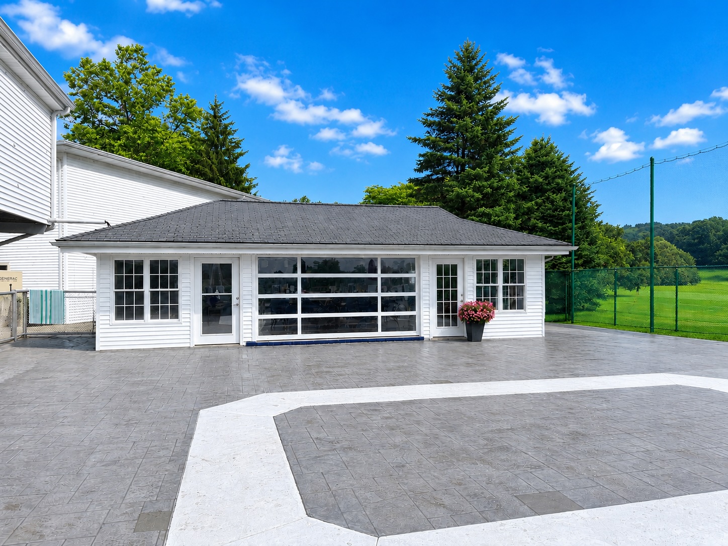 The Brownson Country Club poolside cabana, a white pavilion with large glass doors and windows on a paved patio under a bright blue sky